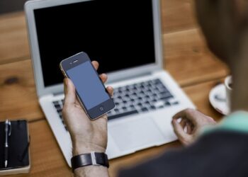 Person holding a smartphone while seated at a laptop